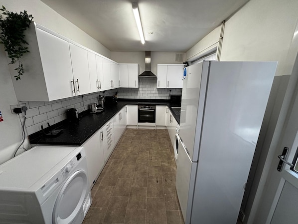 A modern kitchen with white cabinets, a black countertop, a built-in oven, and a washing machine. - Derby Home Stay, Sleeps 4, Near City Centre (Derby)