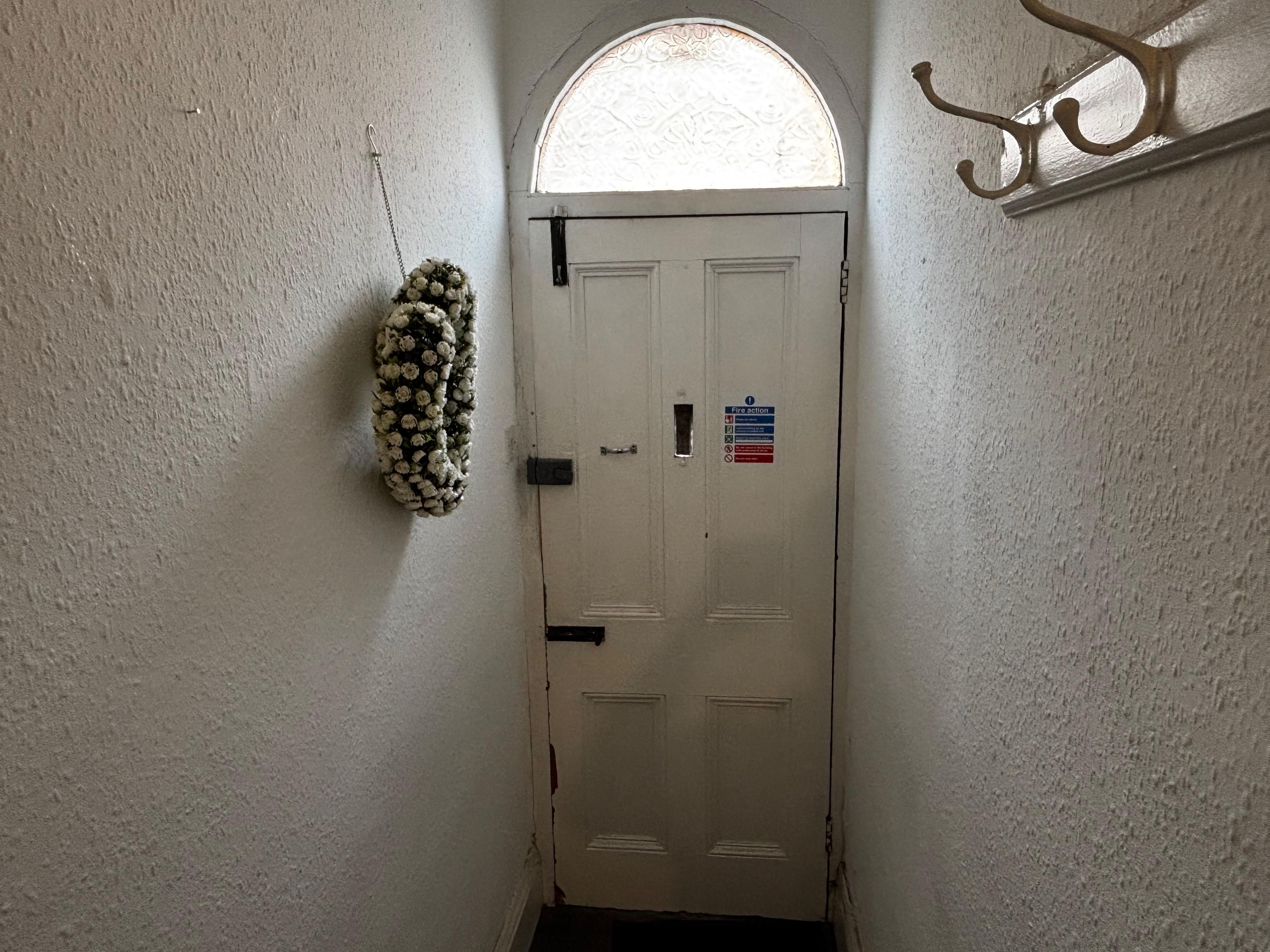 A white door with a fire action sign, a small window above it, and a wall-mounted hook.