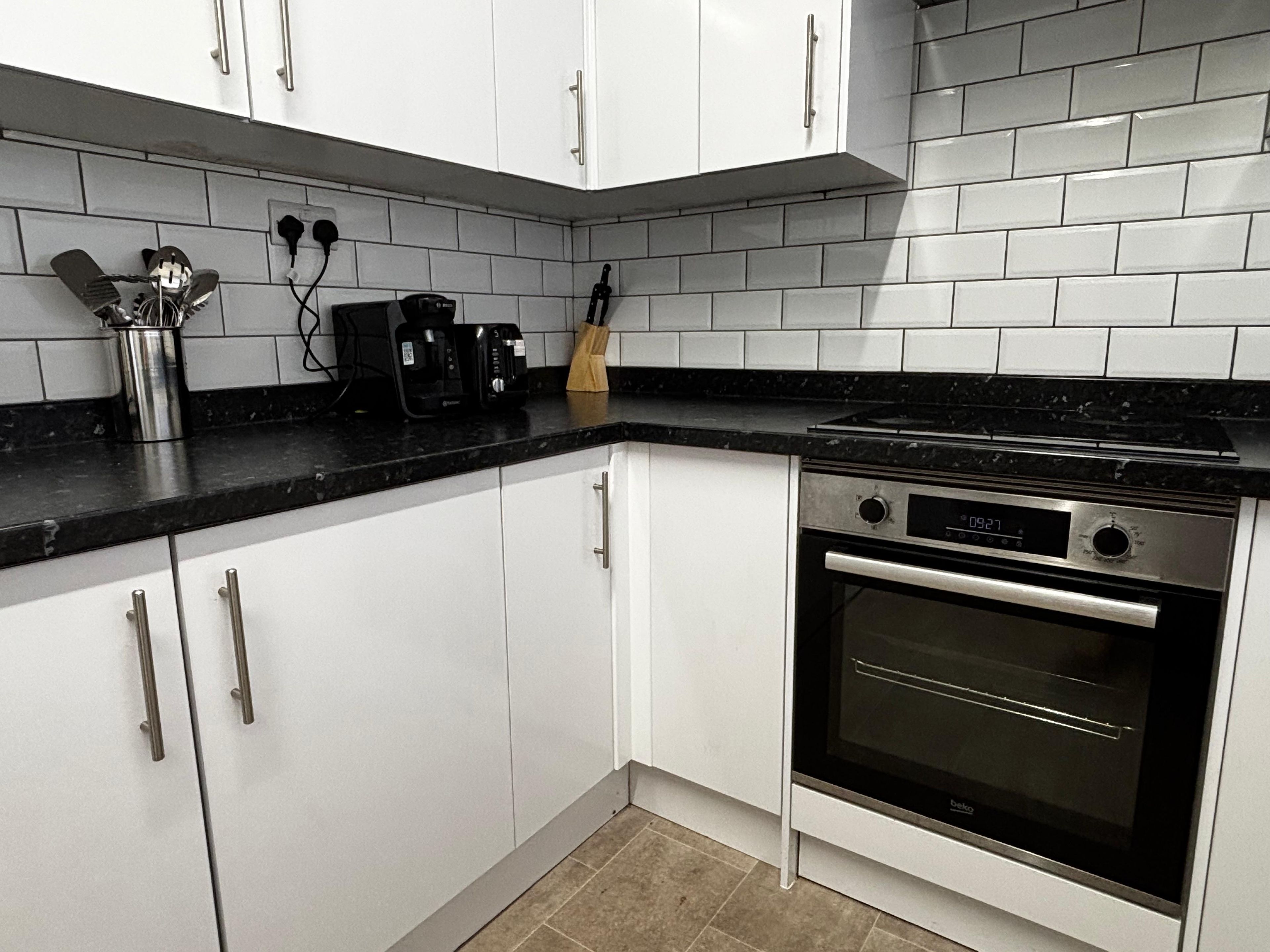 A kitchen with white cabinets, a black countertop, and a built-in oven.