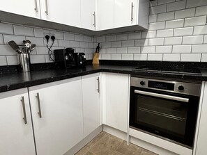 A kitchen with white cabinets, a black countertop, and a built-in oven. - Derby Home Stay, Sleeps 4, Near City Centre (Derby)