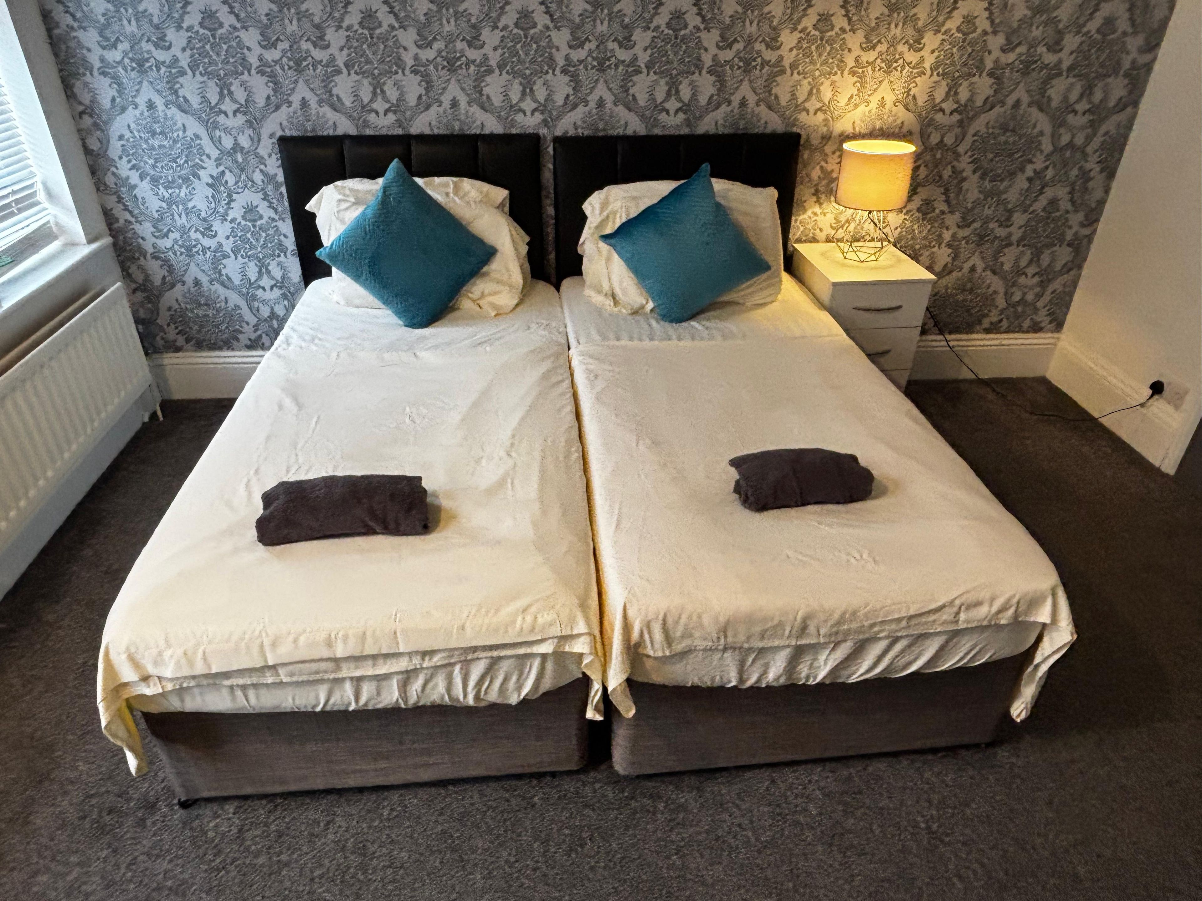 A double bed with a headboard, two pillows, a bedside lamp, and a small bedside table.