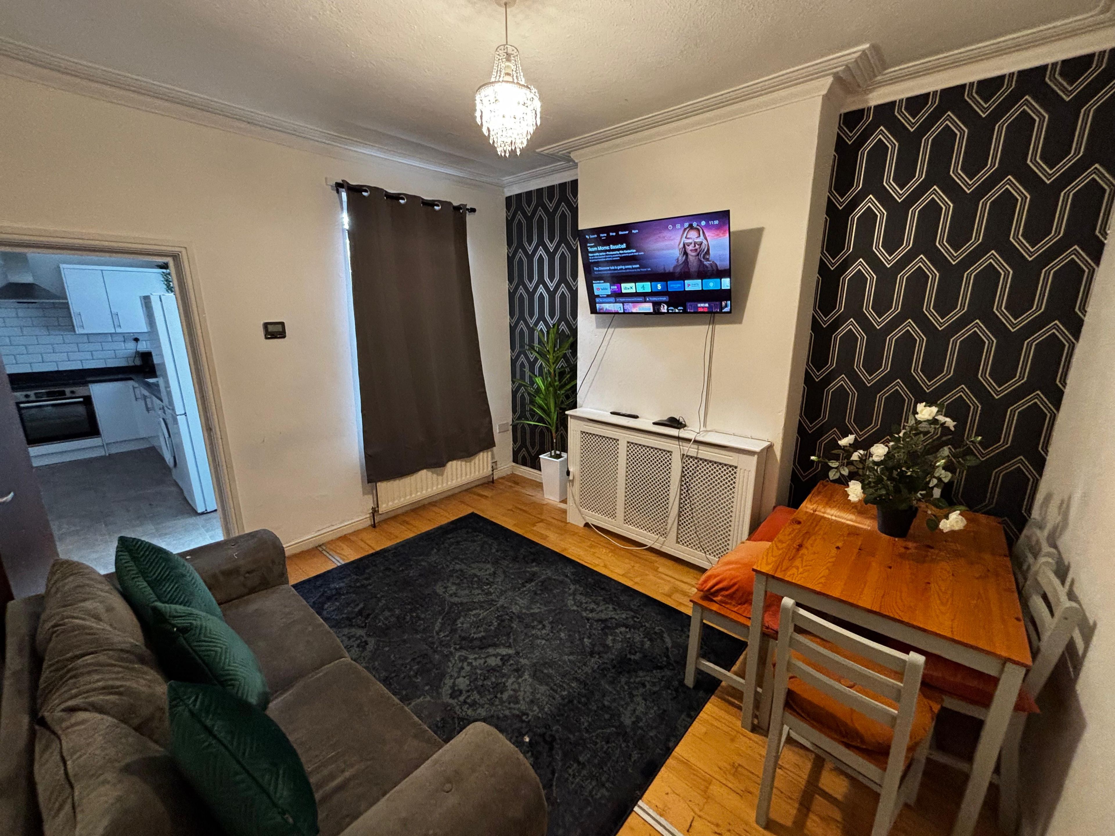 A living room with a sofa, a dining table, a TV, and a patterned wall.