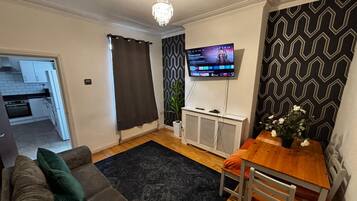 A living room with a sofa, a dining table, a TV, and a patterned wall.