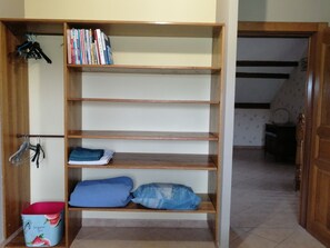 A wooden shelving unit with books, a blue pillow, and a red and white container. - Tortue Accommodation - shared kitchen (Rainville)