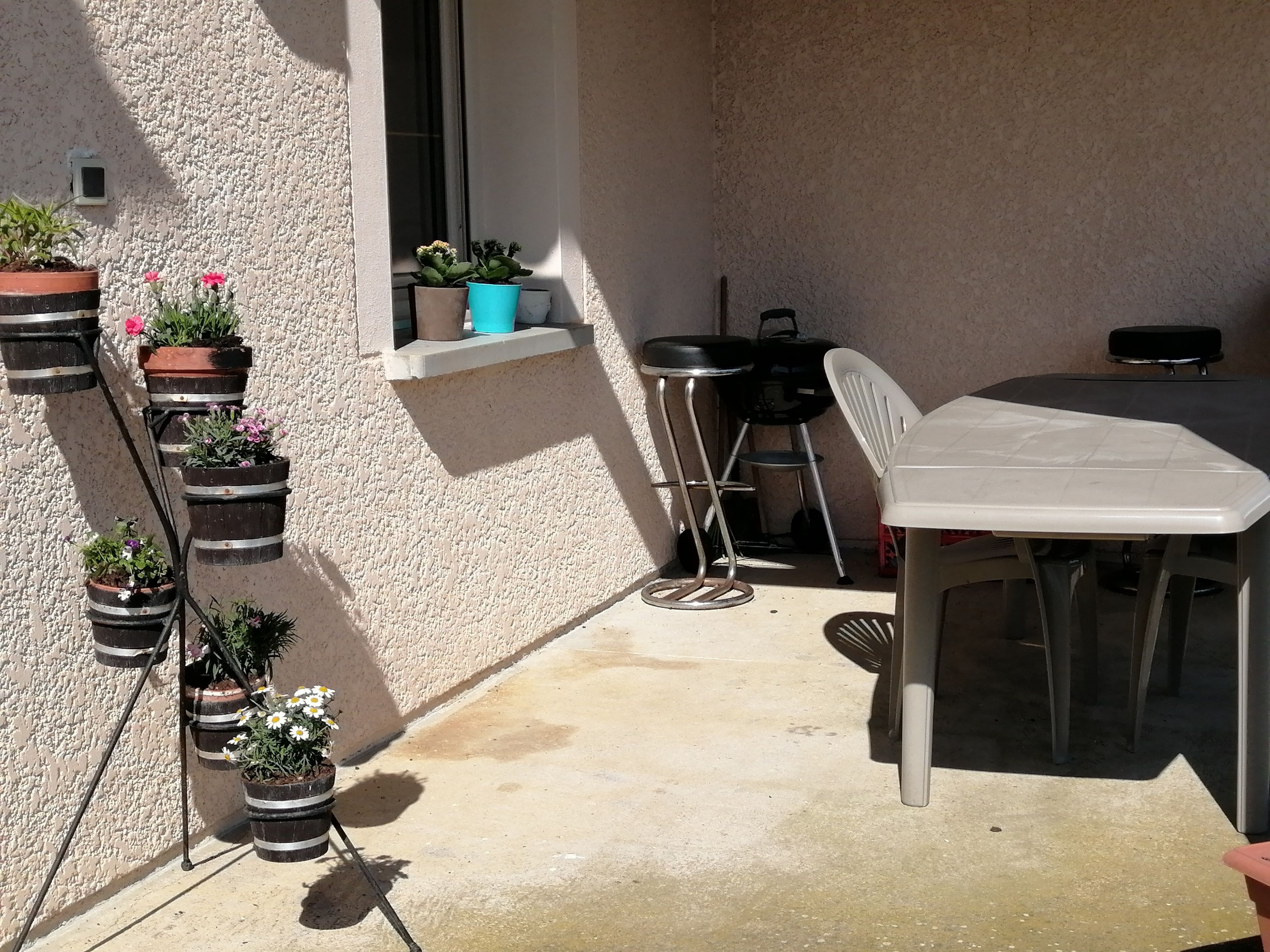 Een terras met een tafel, stoelen, plantenbakken en een klein raam.