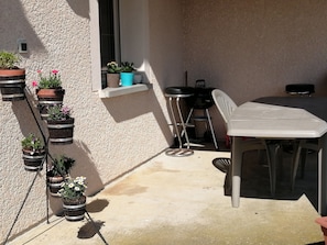 A patio with a table and chairs, potted plants, and a small window.