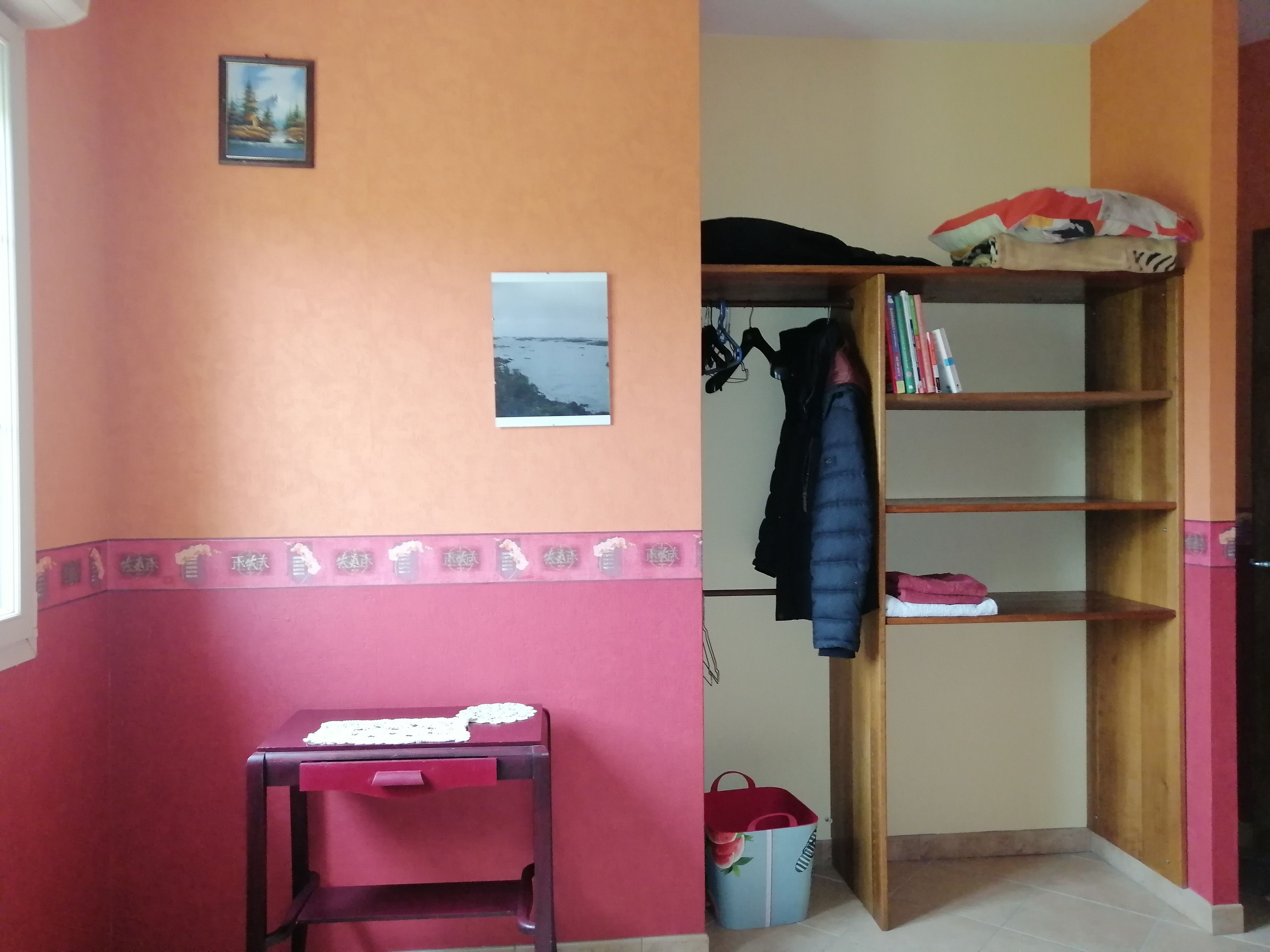 Een kamer met een houten boekenkast, een kleine tafel en een muur met een afbeelding.