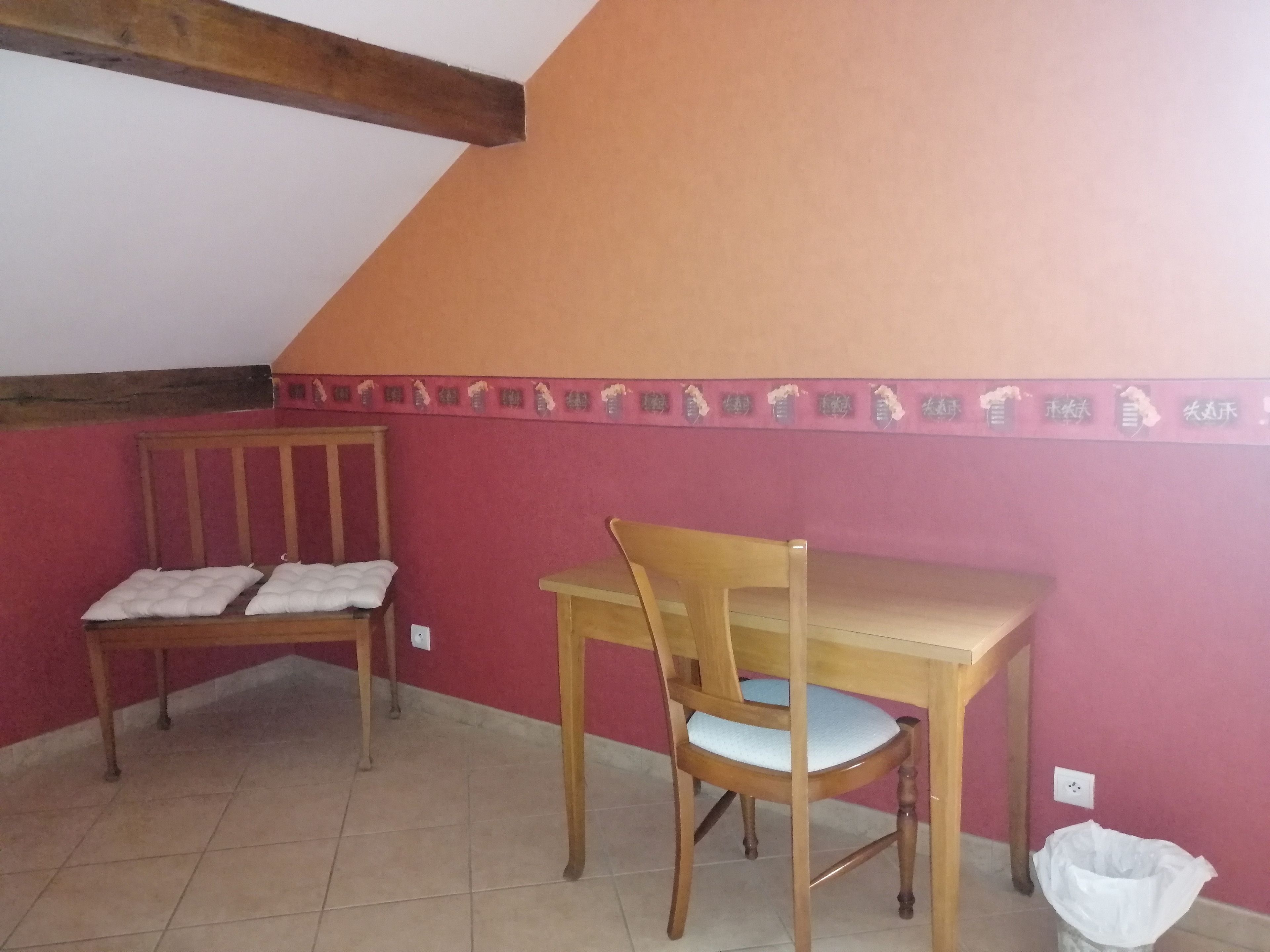 A room with a wooden table and chair, a bench with cushions, and a tiled floor.