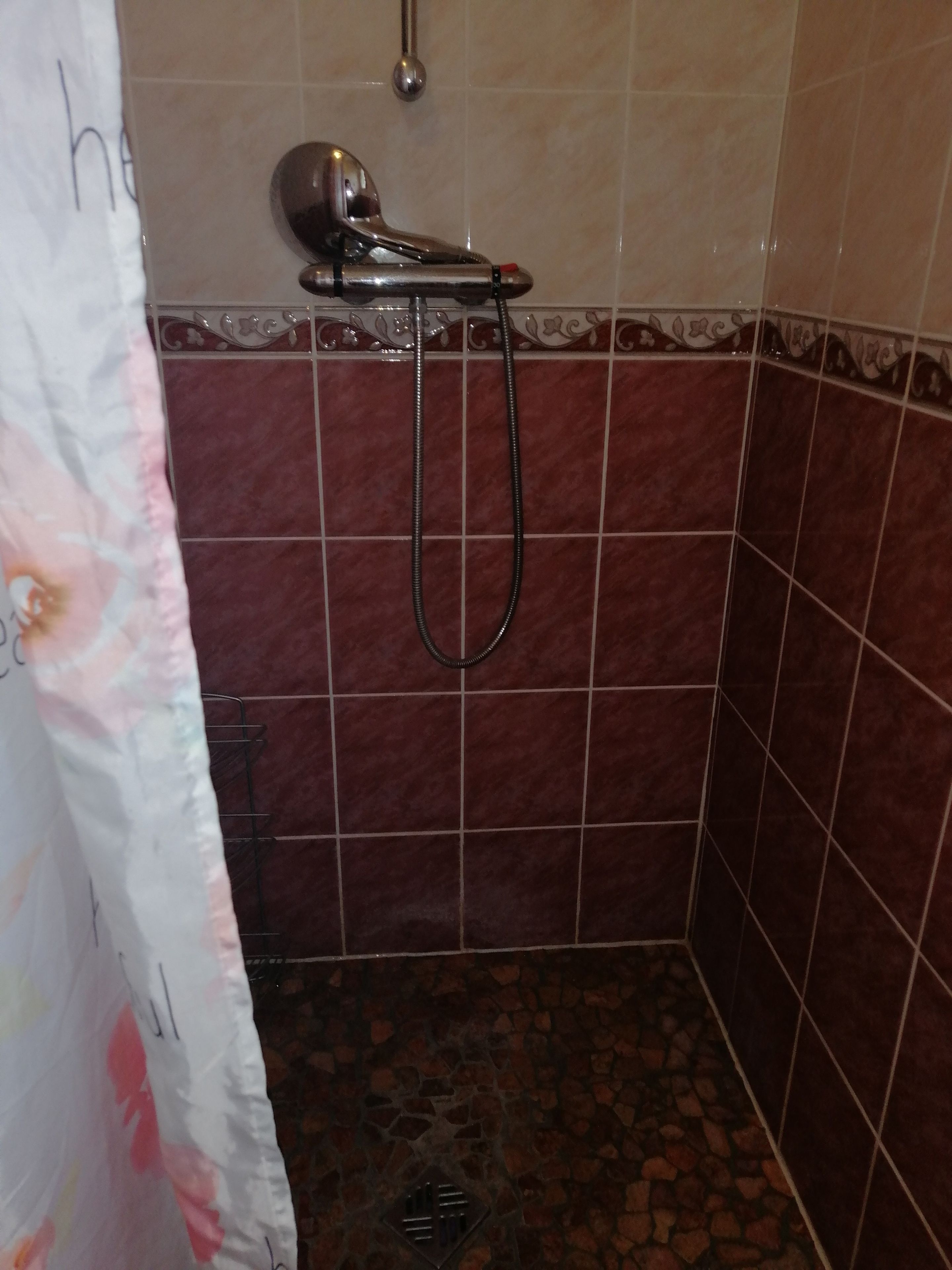 Een badkamer met een douche, betegelde wanden en een gordijn.