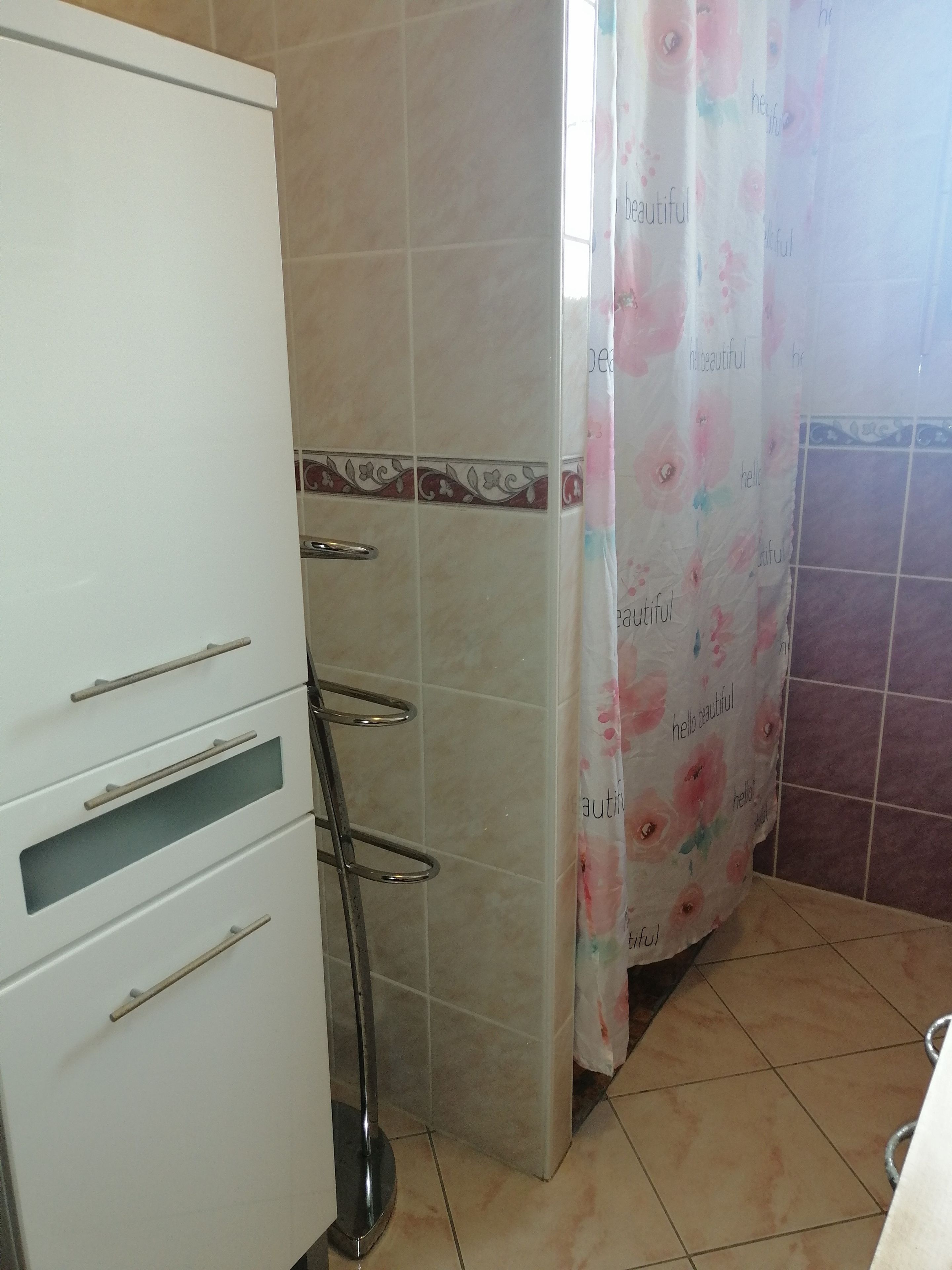 Een badkamer met een wit kastje, een douchegordijn met bloemenmotieven en betegelde wanden.