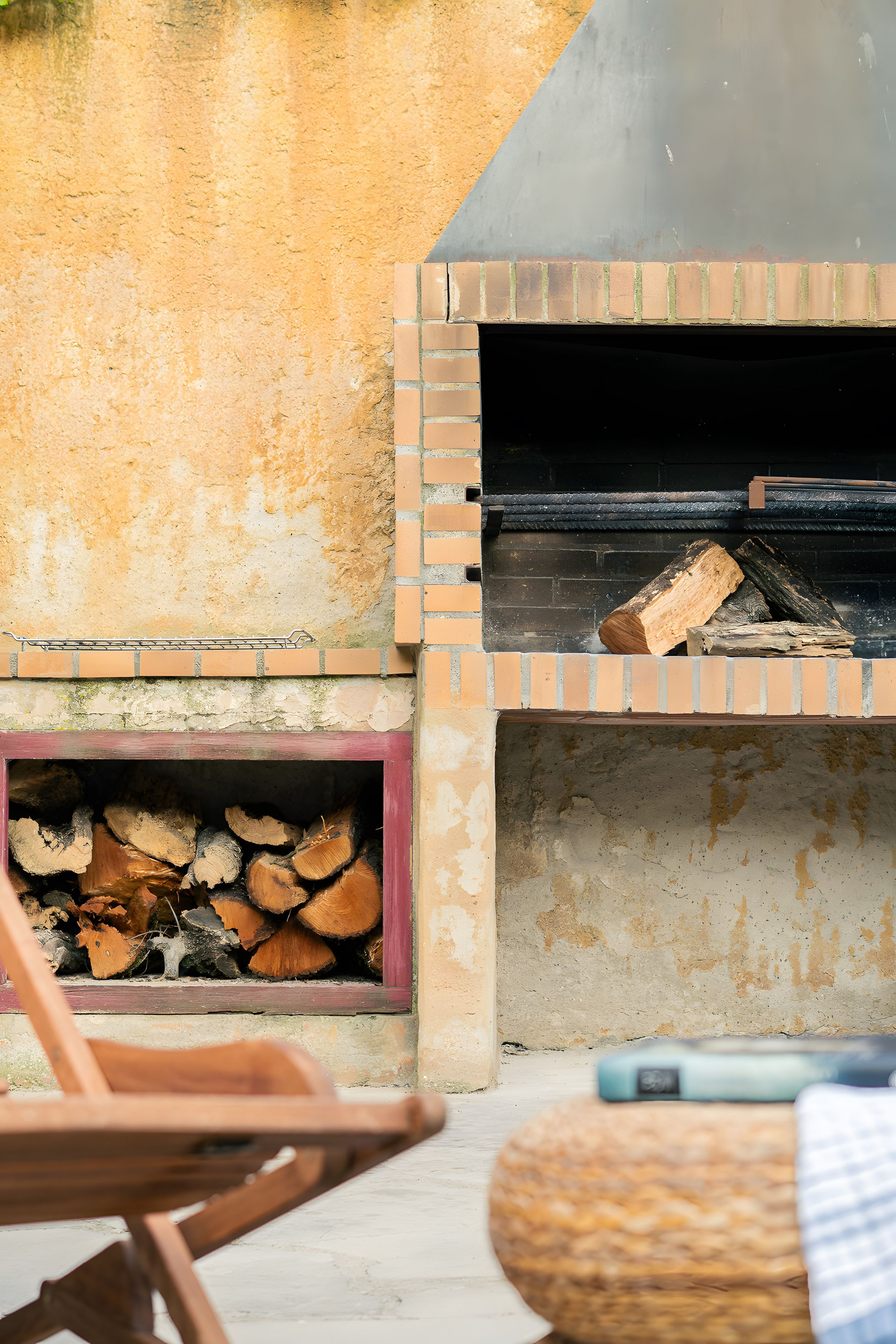 A brick-built outdoor oven with firewood inside, a metal rack, and a wooden chair.