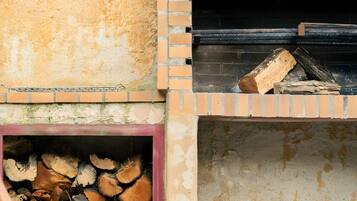 A brick-built outdoor oven with firewood inside, a metal rack, and a wooden chair.