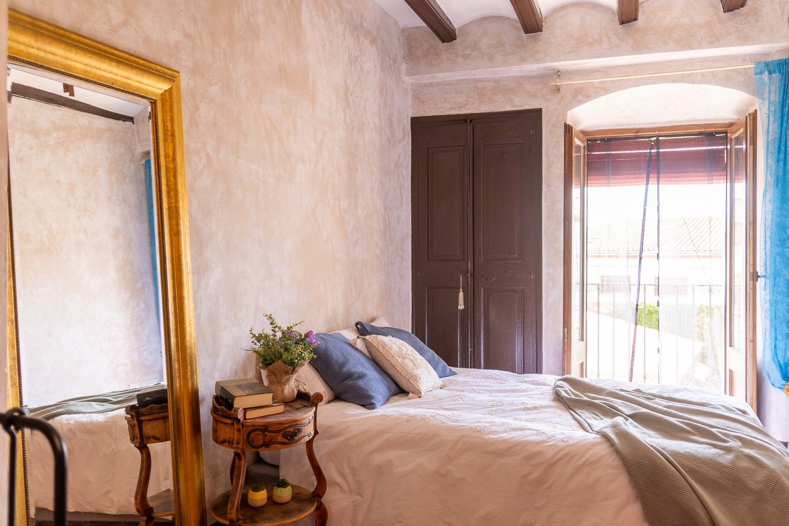 Een slaapkamer met een bed, nachtkastje met boeken, een spiegel en een kledingkast.