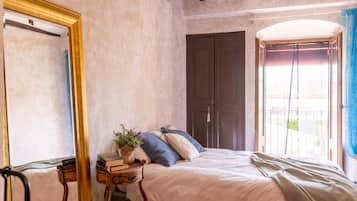 Een slaapkamer met een bed, nachtkastje met boeken, een spiegel en een kledingkast.