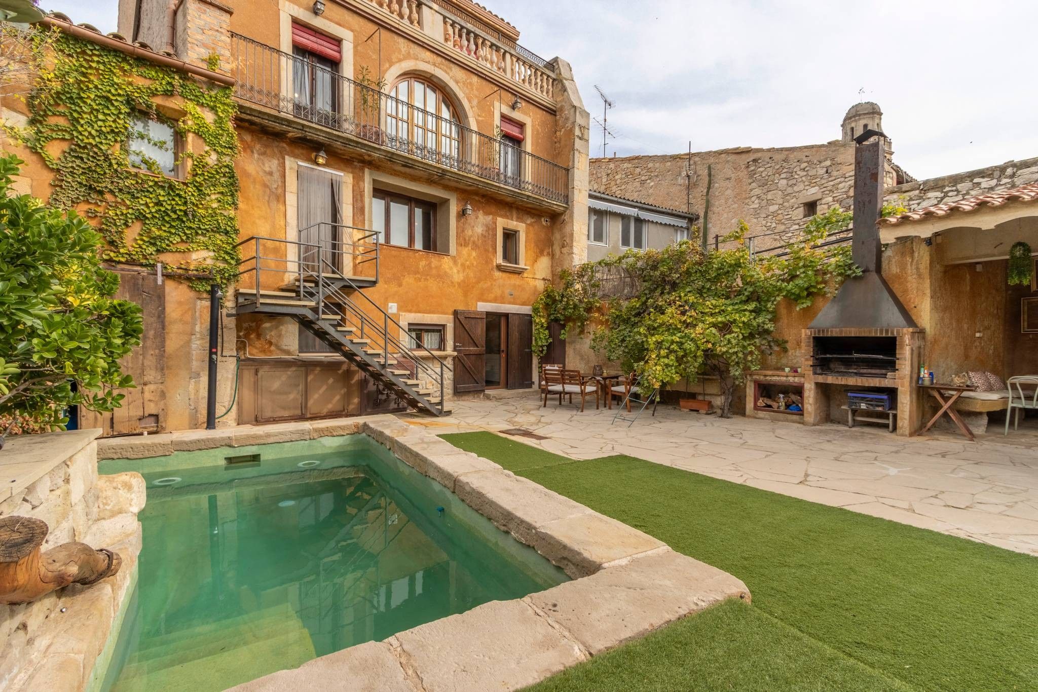 Un patio con piscina, mobiliario exterior y un edificio de piedra con chimenea.