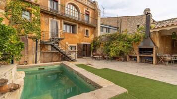 Un patio con piscina, mobiliario exterior y un edificio de piedra con chimenea.