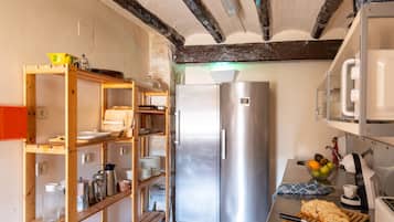 A compact kitchen with a built-in stainless steel refrigerator, wooden shelving, and a small countertop with a toaster and a fruit bowl.