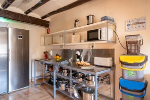 A compact kitchen with a stainless steel refrigerator, a microwave, and a toaster on a shelf. There are pots and pans on shelves below, and a fruit bowl on the counter. - 'Habitació El Niu' with Private Terrace, Kitchen Access, Garden, Pool and Wi-Fi (Sant Martí de Maldà)