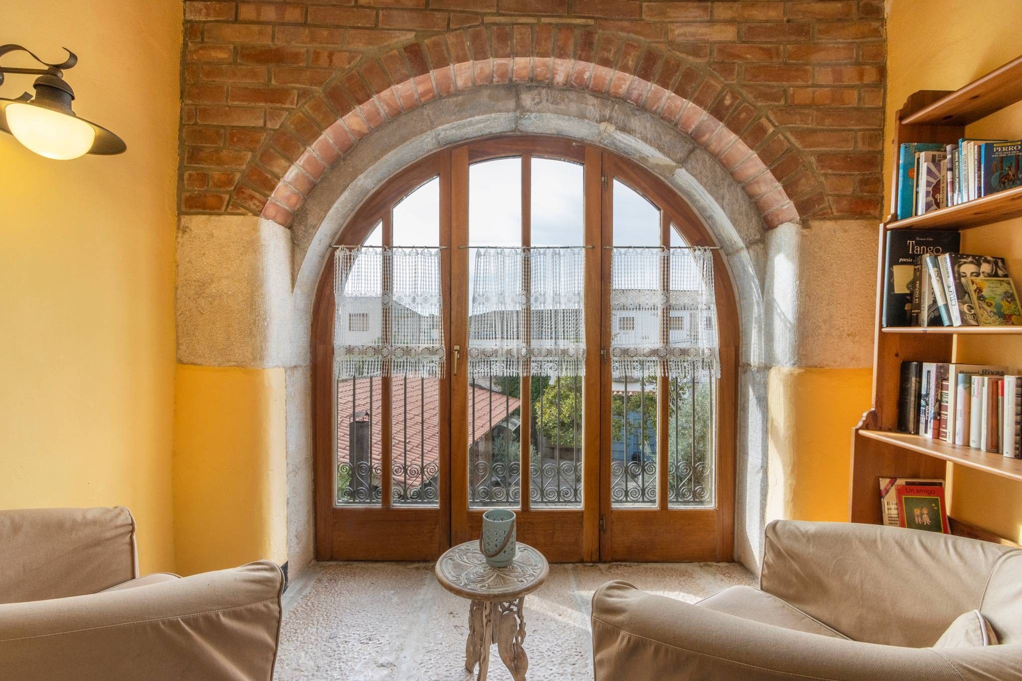 A cozy reading nook with a large arched window, a bookshelf, and two armchairs.