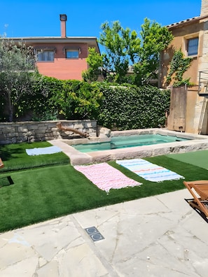 Un pati darrere amb una piscina, gespa artificial i un terra de pedra.