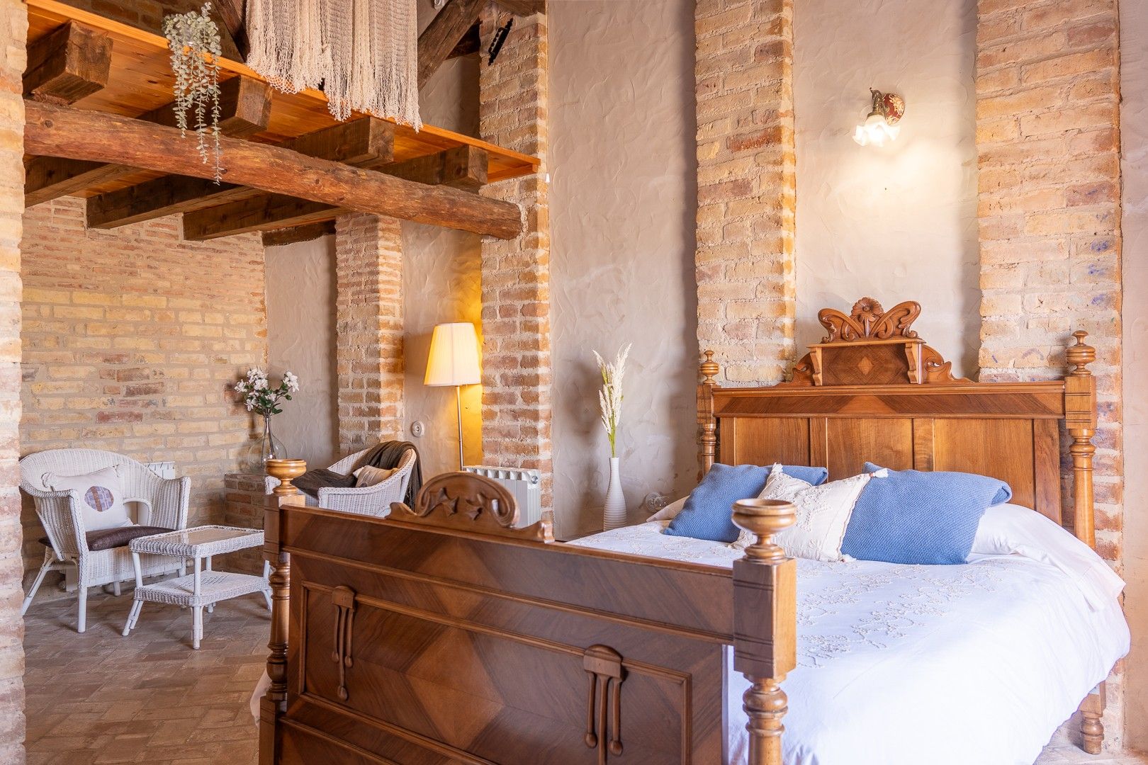Un dormitorio con una cama de madera, una silla, una lámpara y una pared de ladrillo.