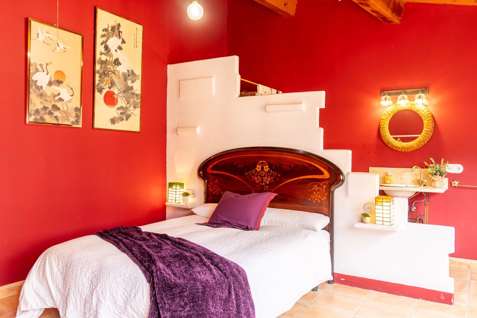 A bedroom with a bed, a nightstand, a wall-mounted shelf, and two framed artworks.