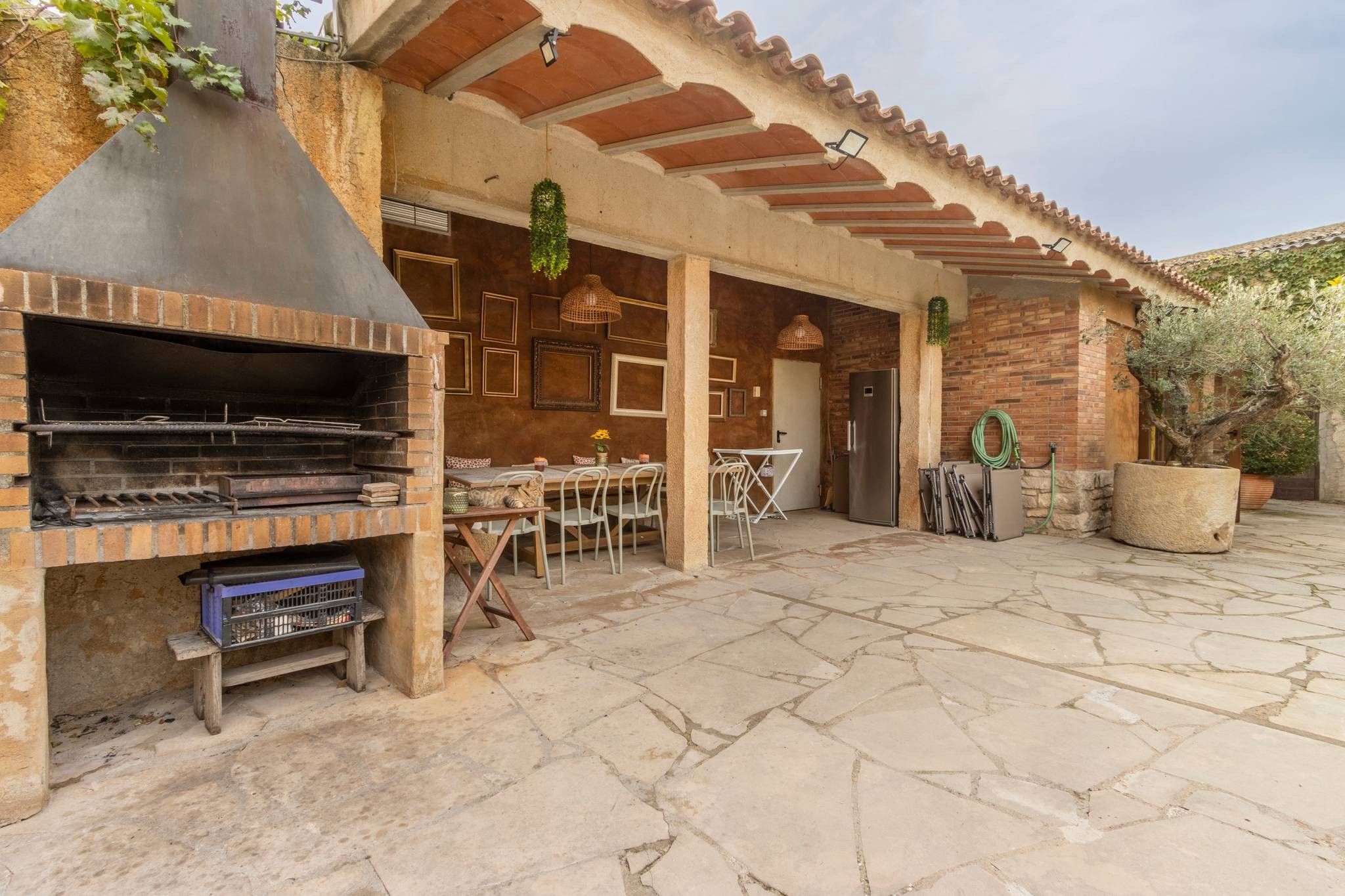Un patio exterior con una parrilla de ladrillo, suelo de piedra y una zona de estar cubierta.