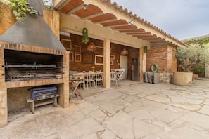 An outdoor patio with a brick barbecue, stone flooring, and a covered seating area. - Room 'La Vinya' with Kitchen Access, Garden, Pool and Wi-Fi (Sant Martí de Maldà)