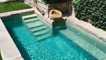 Piscina rectangular con agua azul cristalina, rodeada de muros de piedra y abundante vegetación.