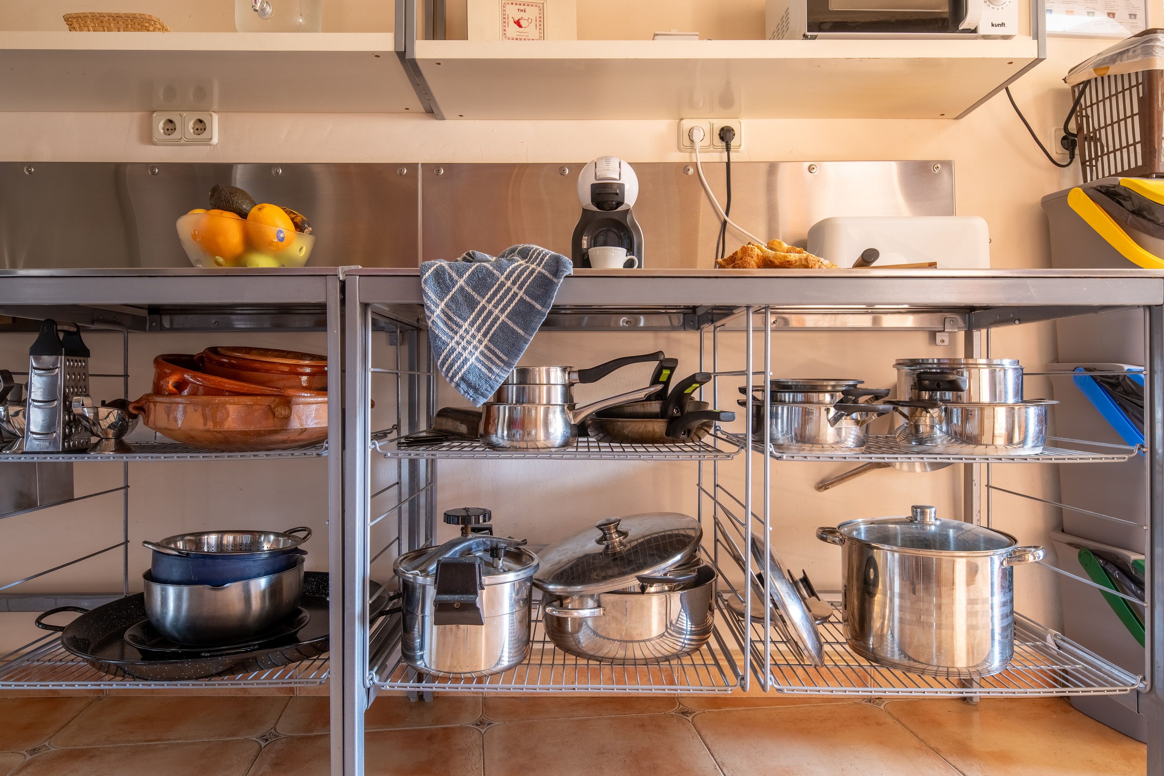 Een keuken met roestvrijstalen apparatuur, een koffiezetapparaat en verschillende pannen en potten op planken.