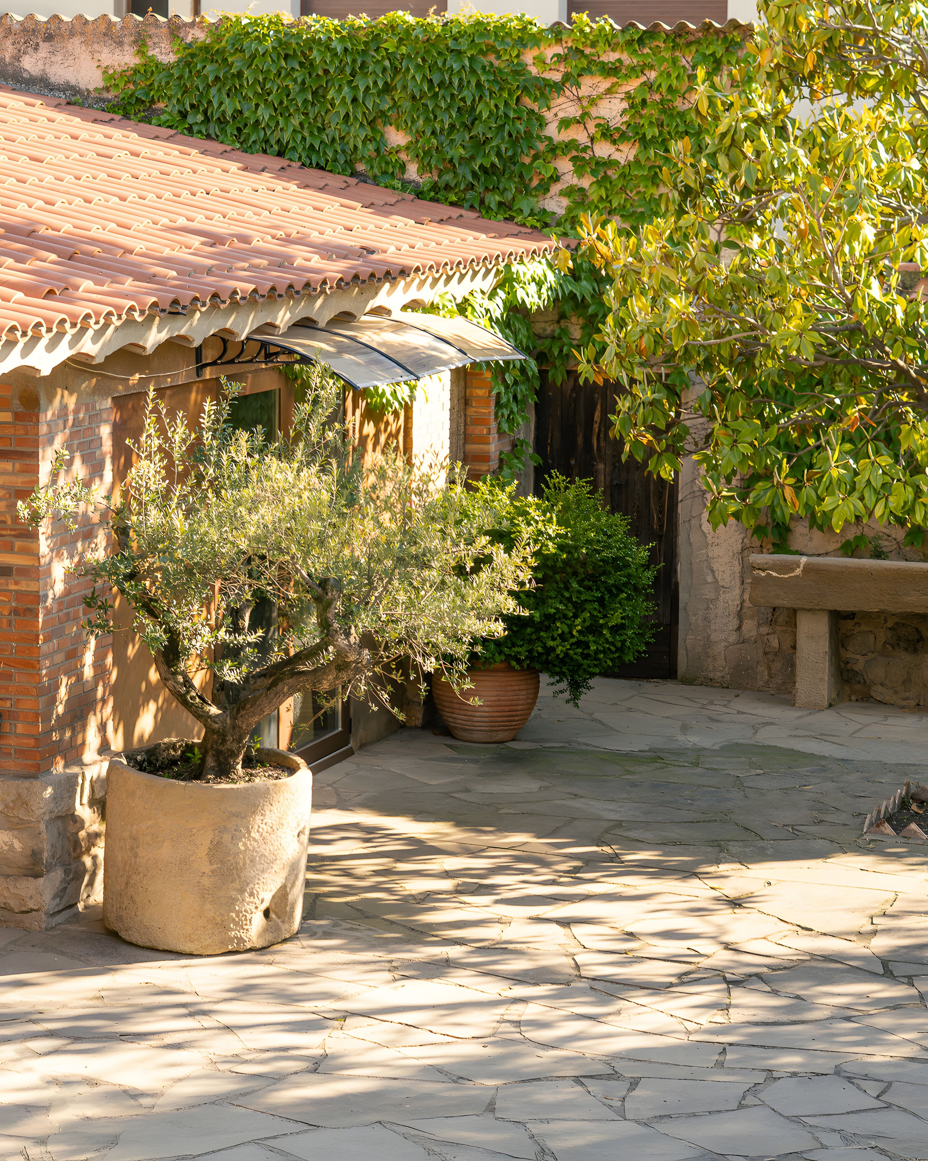 A courtyard with a tiled roof, potted plants, and a stone bench.