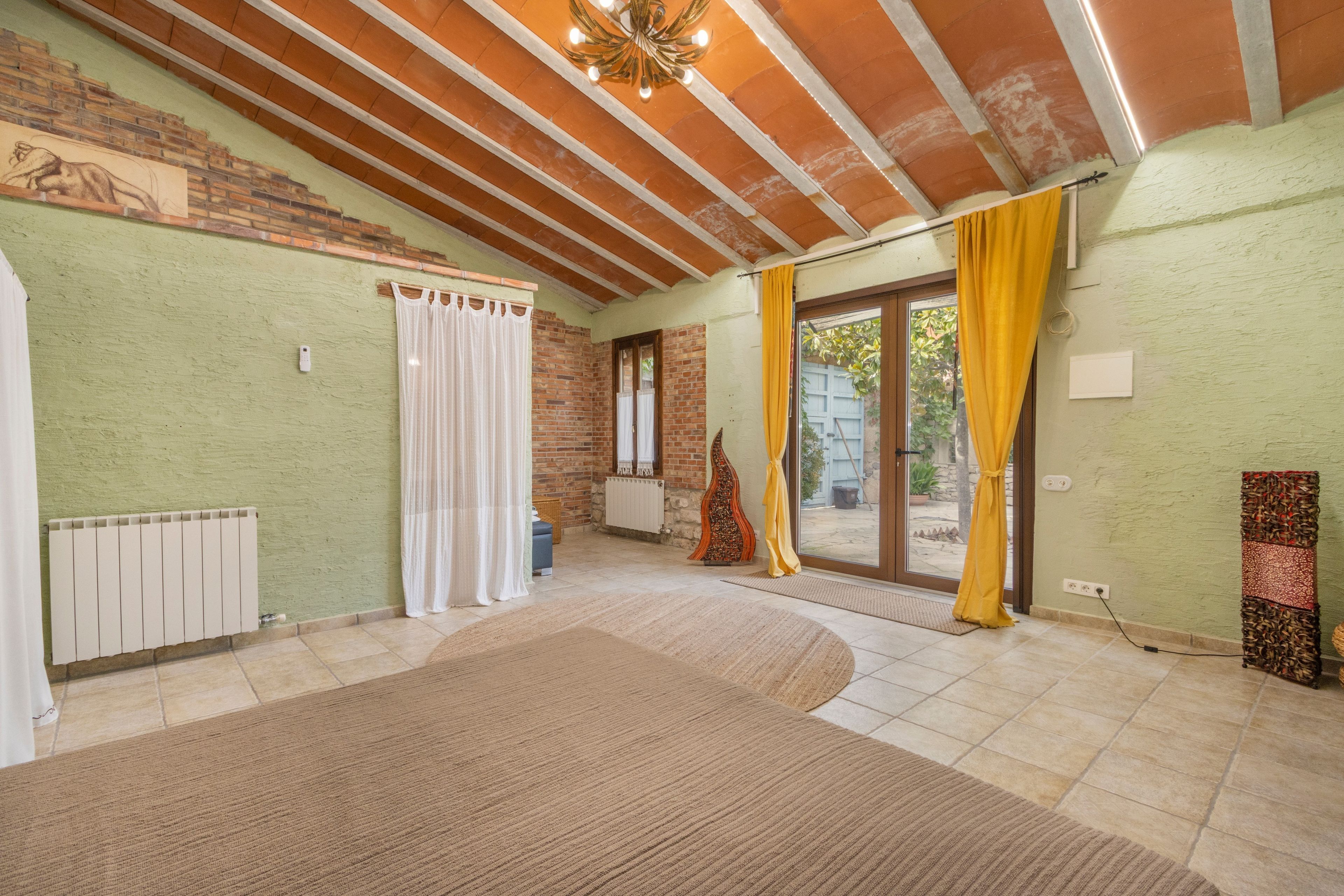 A spacious room with a sloped ceiling, a radiator, a window with curtains, and a door leading outside.