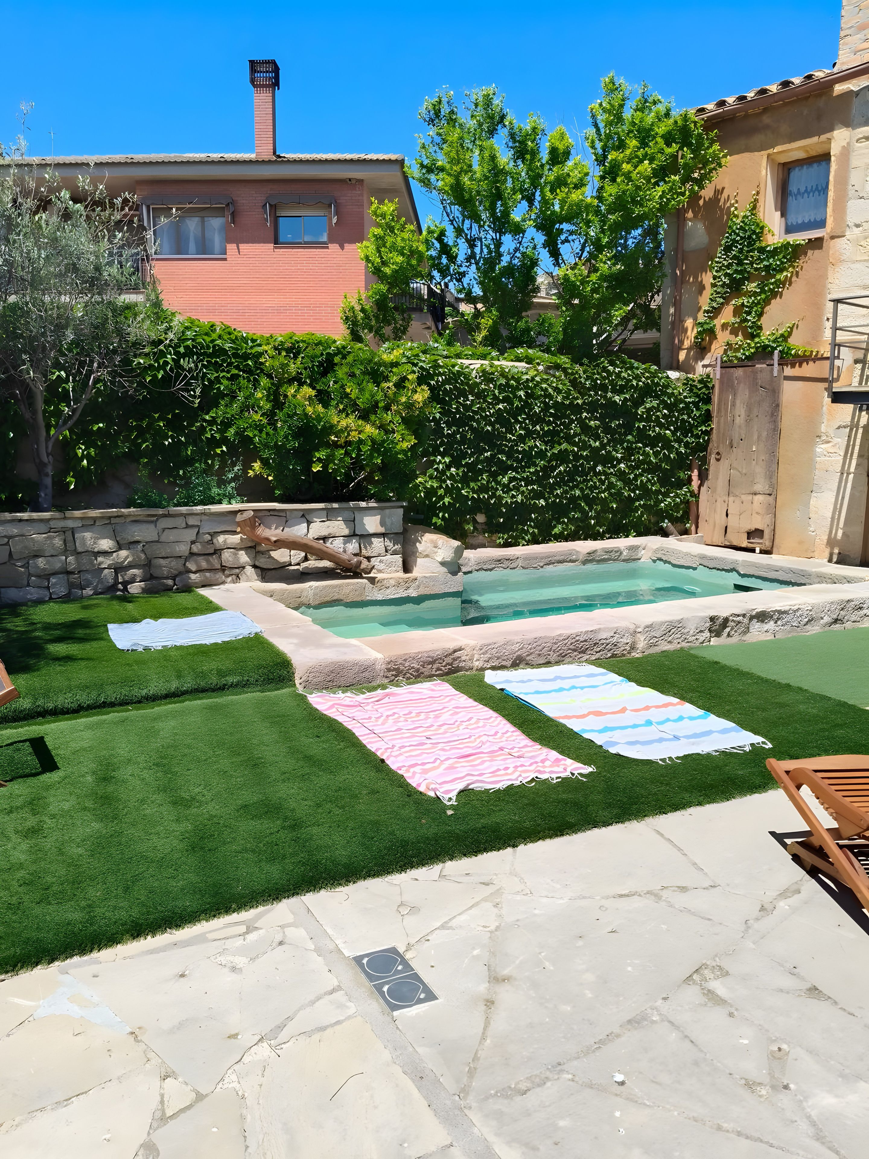 A backyard with a swimming pool, artificial grass, and a stone patio.