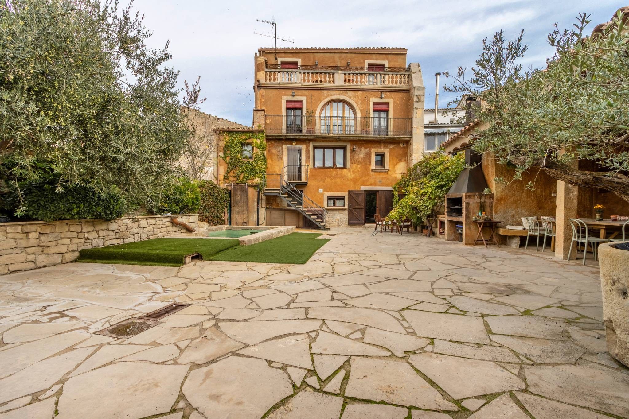A courtyard with a stone floor, a staircase leading to a second floor, and a dining area with outdoor seating.