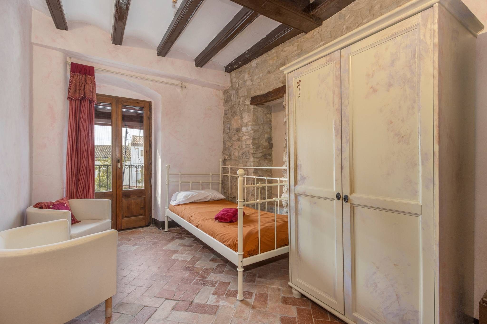 A bedroom with a bed, a wardrobe, a chair, and a window with curtains.