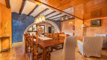 A dining area with a wooden table and chairs, a chandelier, and a view through an arched doorway.