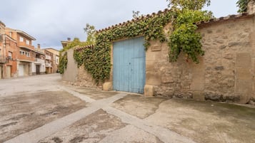 A narrow street with a blue door, stone walls, and a building with a tiled roof.