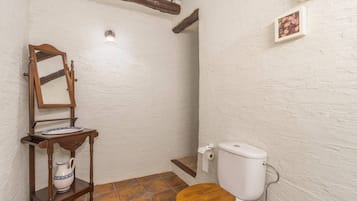 Un baño pequeño con inodoro de madera, un espejo, una repisa con jarrón y un dispensador de papel higiénico.