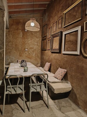Una habitación rústica con un banco de piedra, una mesa con sillas y una lámpara colgante.