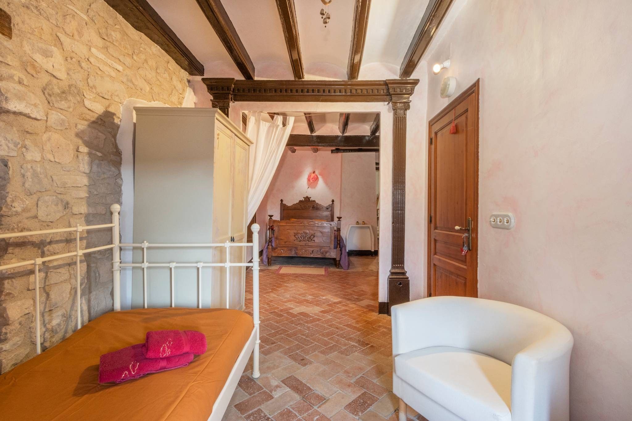 Un dormitorio con cama, una silla, un armario y una pared de piedra.