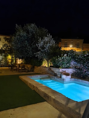 Una piscina con borde de piedra, rodeada por un muro de piedra y follaje.