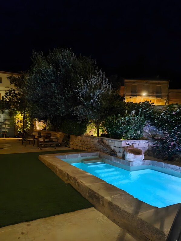 Una piscina con borde de piedra, rodeada por un muro de piedra y follaje.
