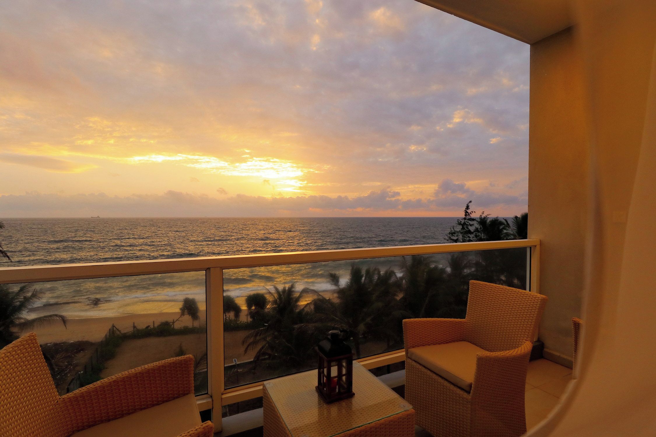 Un balcone con mobili in vimini e vista sull'oceano al tramonto.