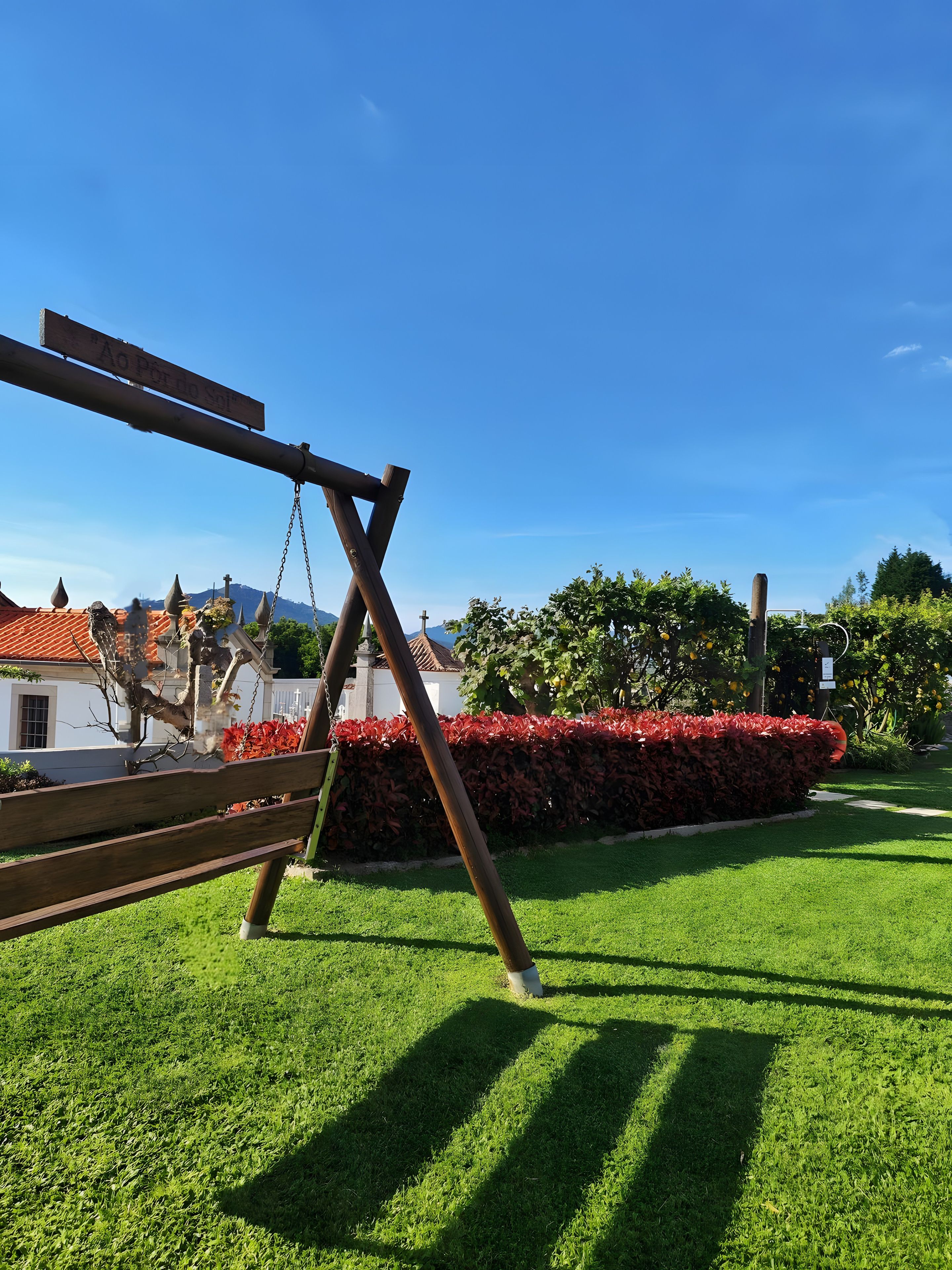 A wooden swing set in a well-maintained grassy area with a hedge and a clear sky.