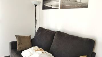 A living room with a dark grey sofa, a lamp, and two black and white beach photographs on the wall.