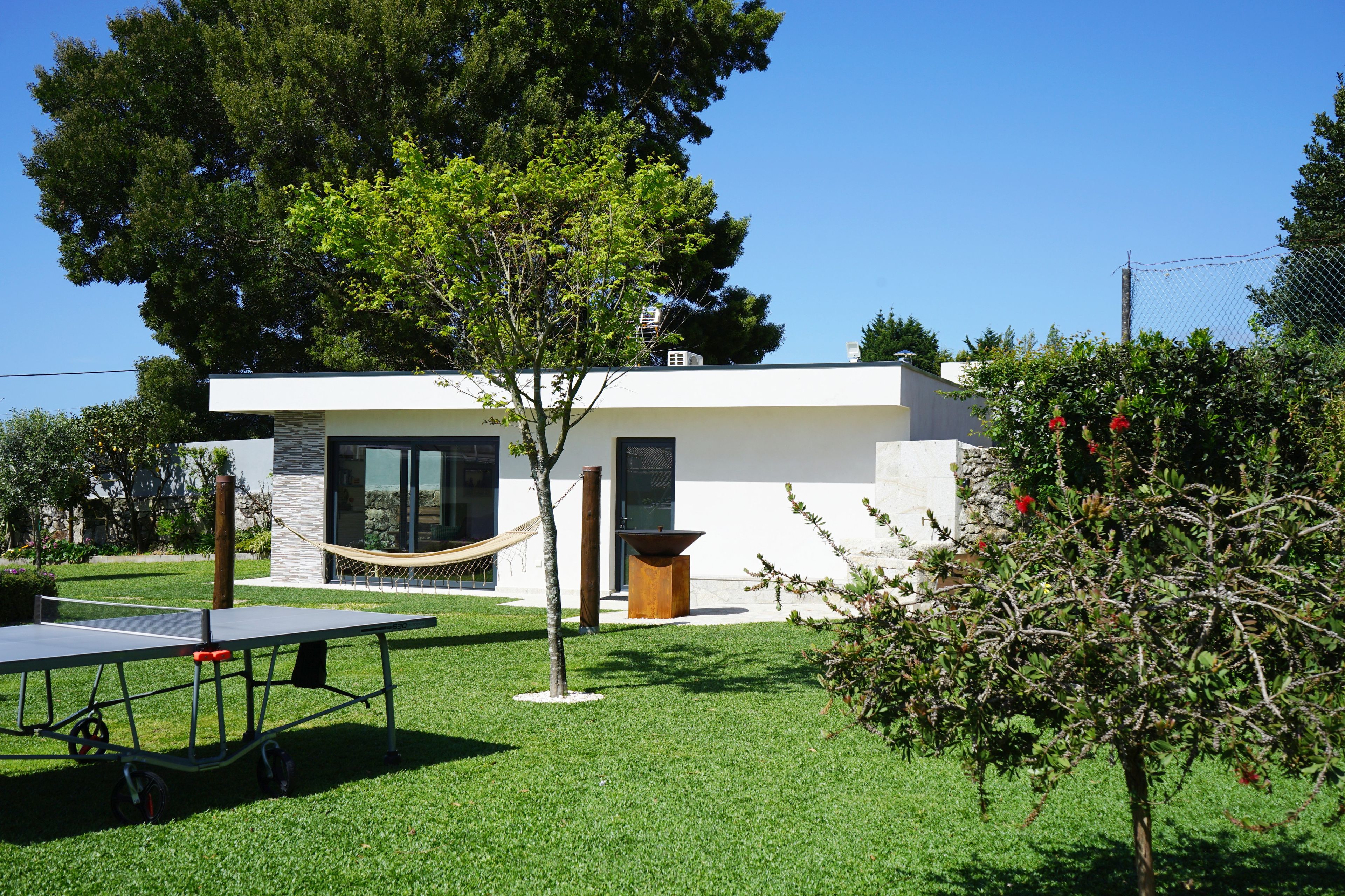 Ein modernes Haus mit kleinem Garten, einer Hängematte und einem Tischtennis-Tisch.