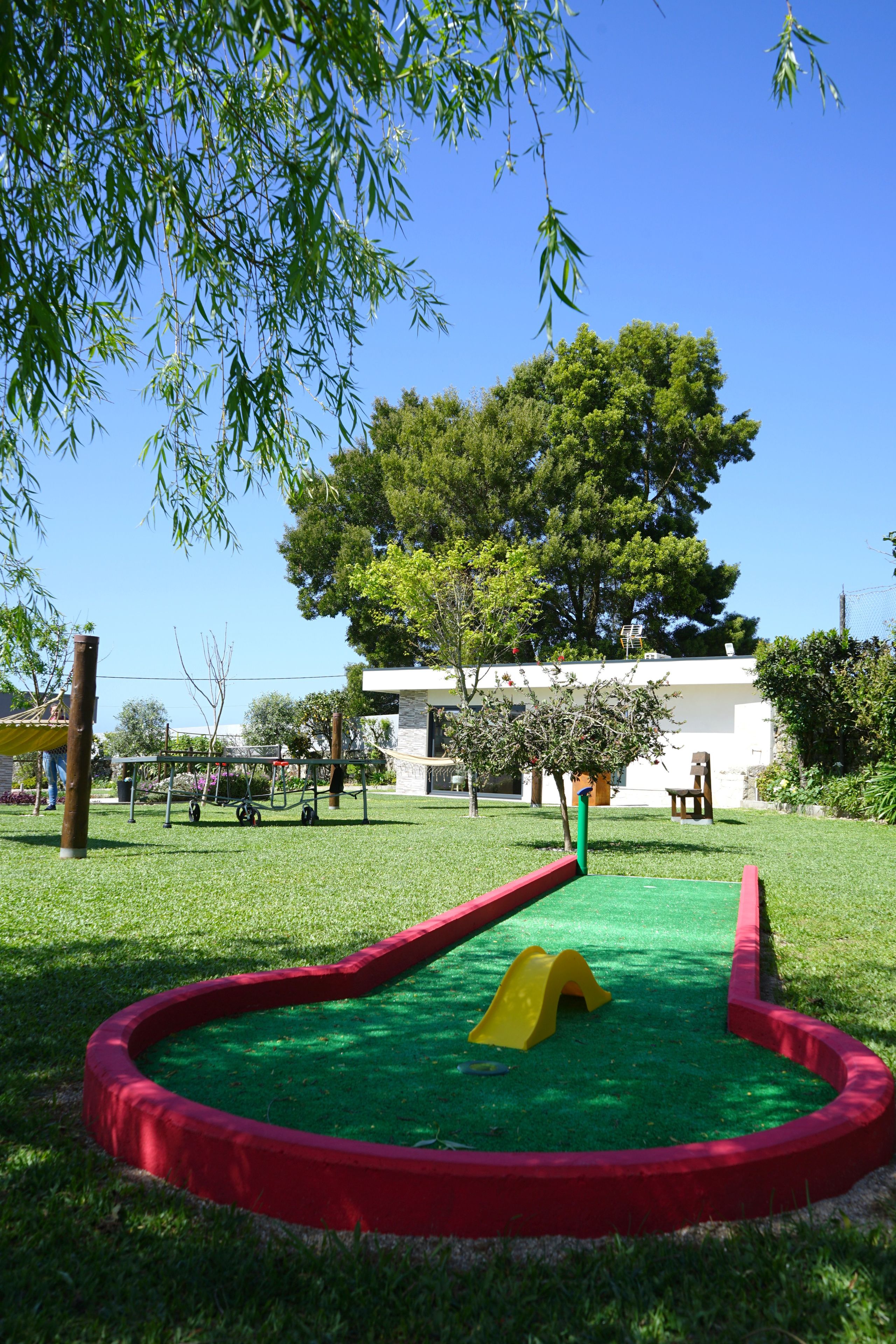 Un parque infantil con tobogán y zona de escalada, rodeado de césped y árboles.