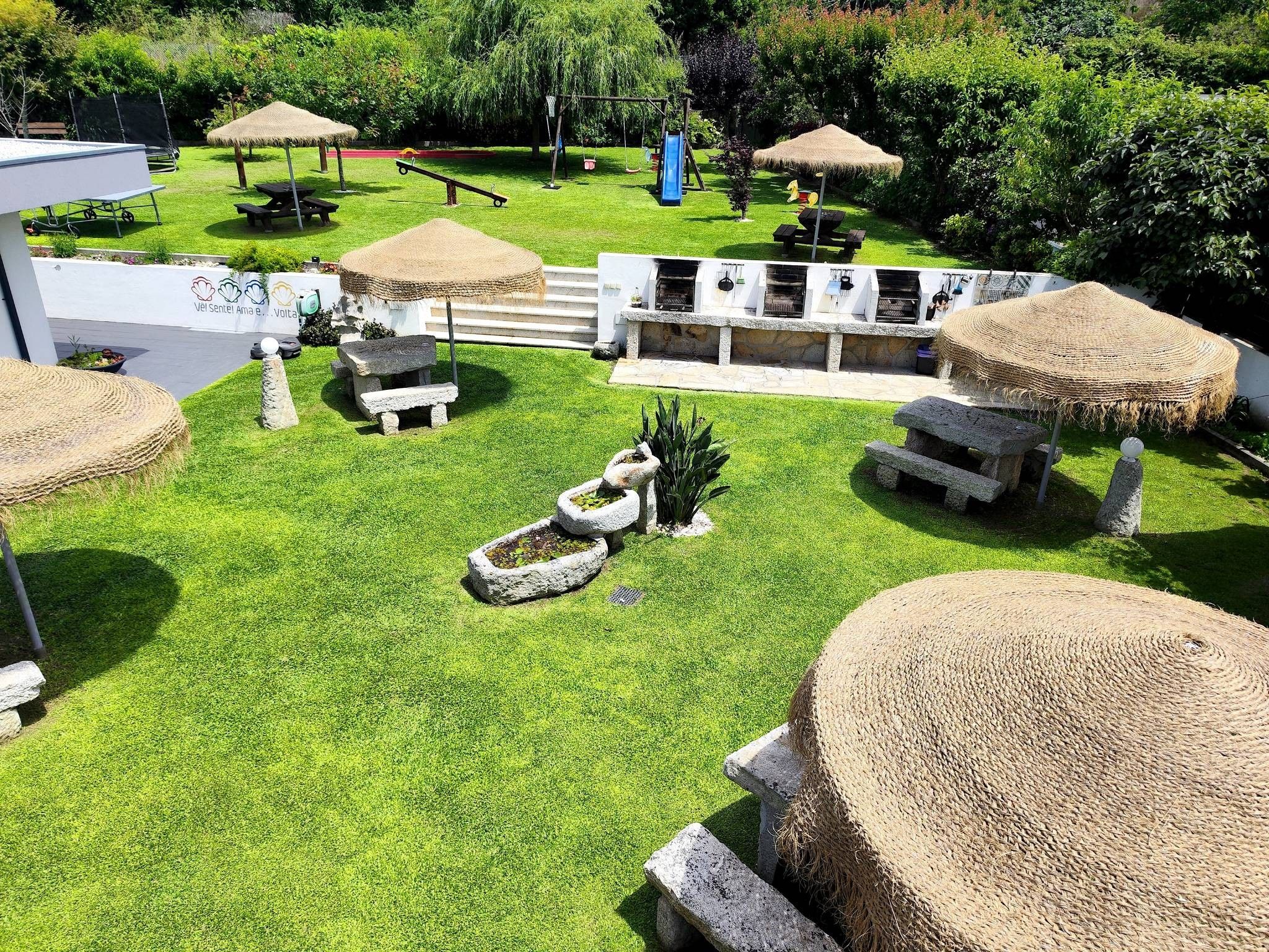 A well-maintained outdoor area with a grassy lawn, stone benches, and thatched umbrellas.