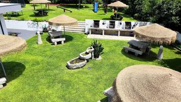 A well-maintained outdoor area with a grassy lawn, stone benches, and thatched umbrellas.