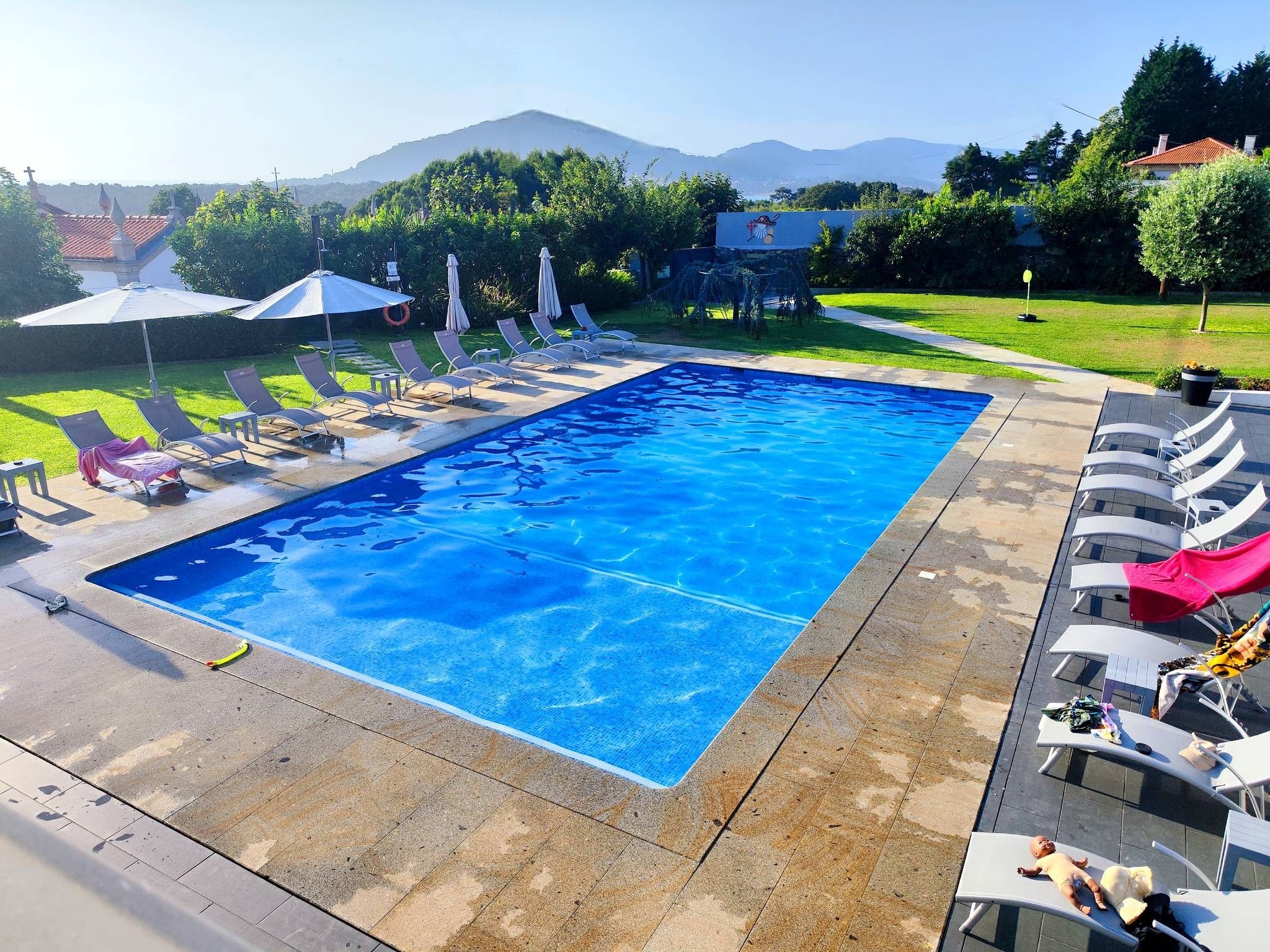 Una piscina rectangular amb aigua transparent i blava, envoltada de gandules i ombrel·les.